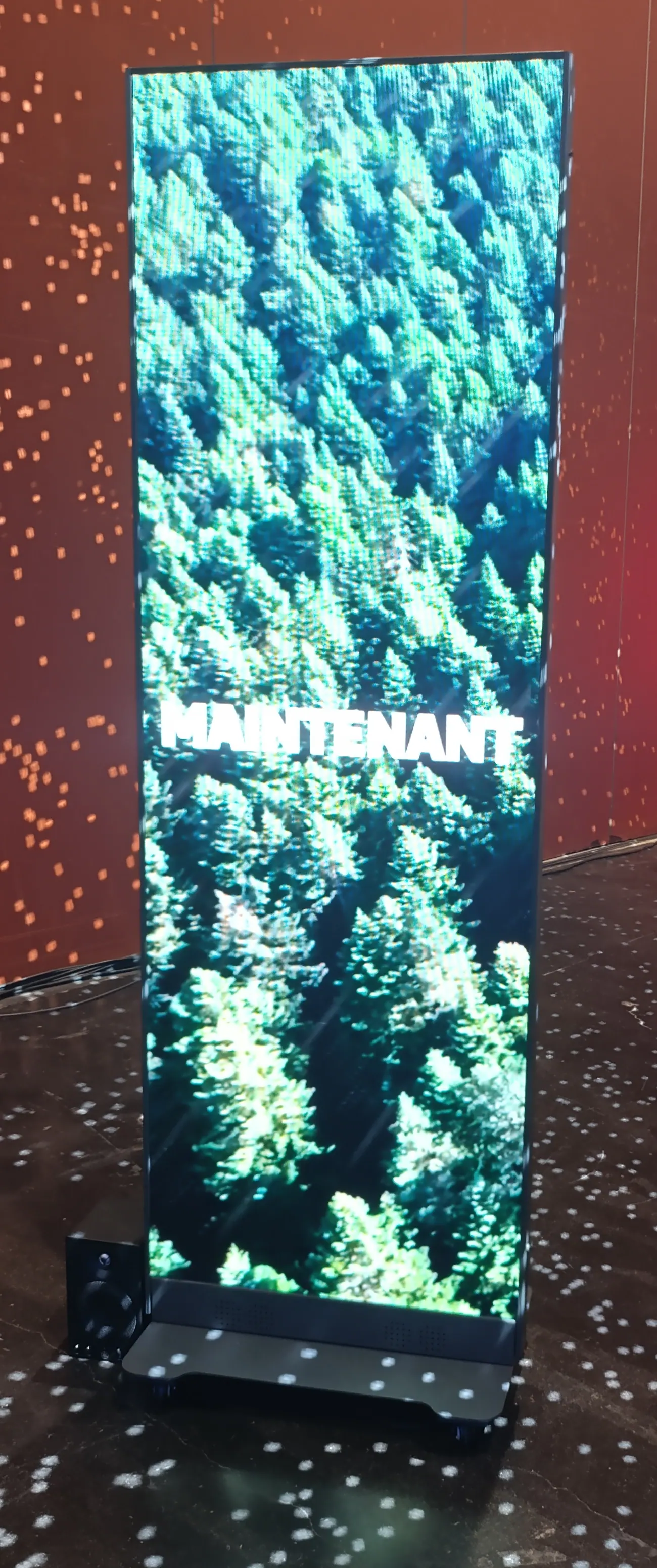 Totem LED vertical sur son socle, diffusant une image de forêt dans un espace événementiel.